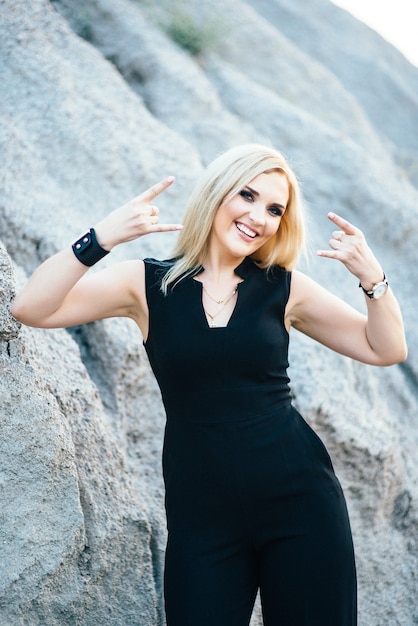 Blonde girl in a black trouser suit with blue eyes on the background of a granite quarry from gray rubble