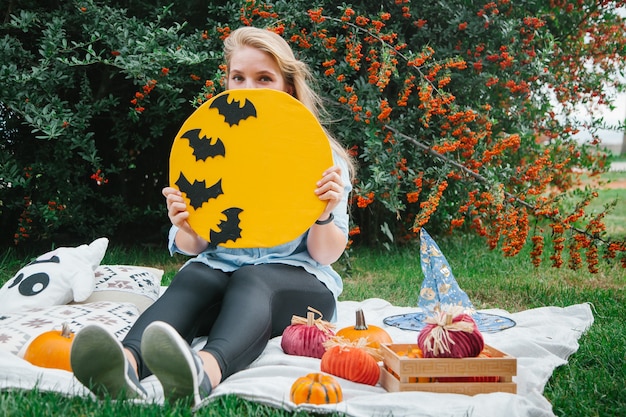 Blonde girl on the blanket in the park on the lawn with a ghost and pumpkins Halloween symbols