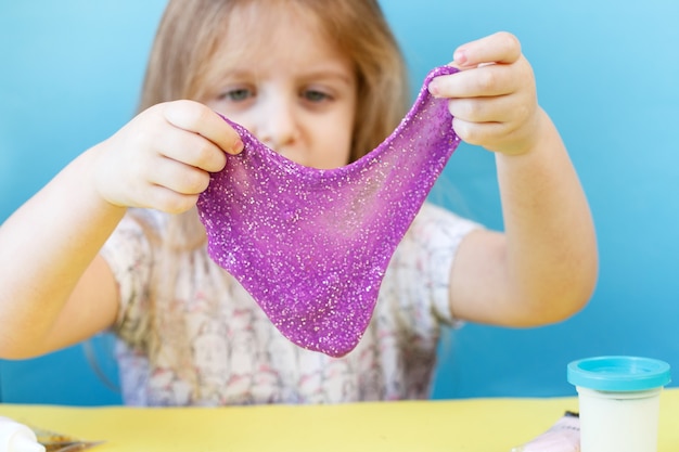 Blonde girl hold and stretching purple glitter slime child playing with a slime toy