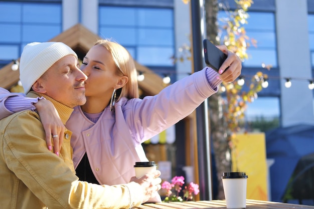 A blonde girl holds a phone and takes a selfie with her boyfriend Girl kissing a guy