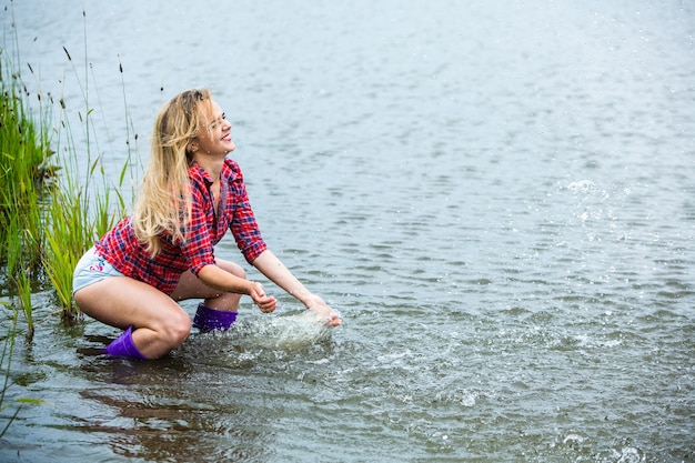 The blonde girl is having fun in the river in rubber boots in the country