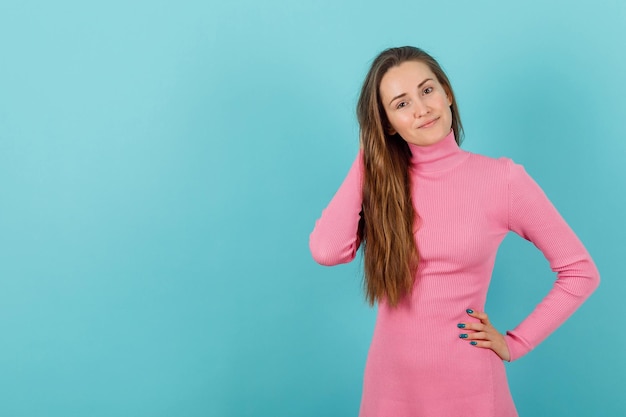 Blonde girl is holding one hand behind head and other on waist on blue background