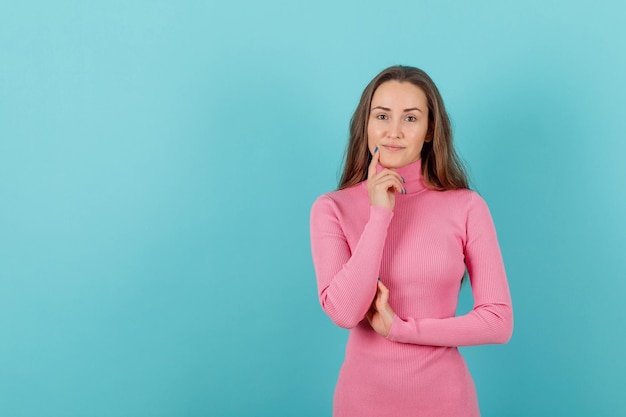 Blonde girl is thinking by holding forefinger on chin on blue background