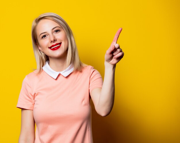 Blonde girl in pink dress show gesture on yellow space