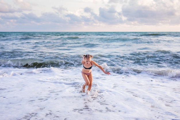 Blonde girl running and jumping on the beach on blue sea shore in summer vacation at the day time. 