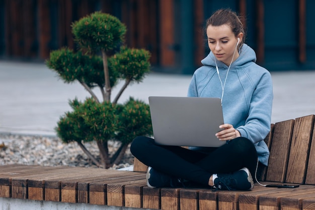 Blonde girl sitting on bench in park holding laptop