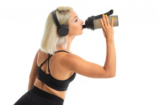 Blonde girl in a sports uniform drinks water listens to music