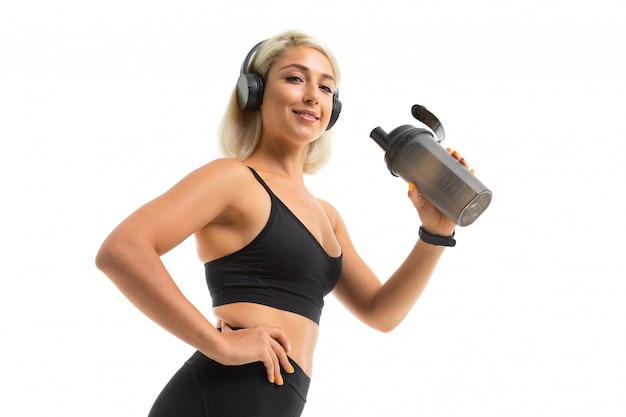 Blonde girl in a sports uniform holds a water bottle and listens to music