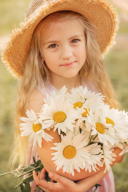 a blonde girl in a straw hat holds a bouquet of white daisies in her hands