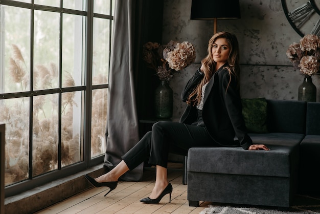 A blonde girl in a suit is sitting on the couch