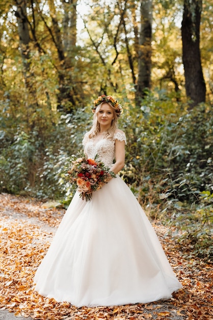 Blonde girl in a wedding dress in the autumn forest