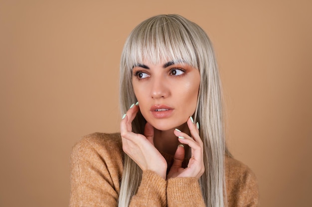 Blonde girl with bangs and brown daytime make-up in a sweater on beige background sensual fashion portrait