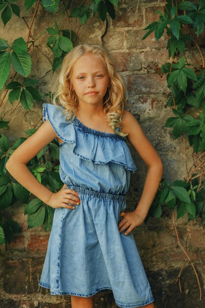 Blonde girl with curly hair posing against the wall with wild grape leaves. High quality photo