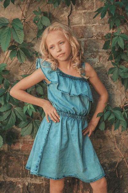 Blonde girl with curly hair posing against the wall with wild grape leaves. High quality photo