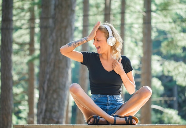 Blonde girl with headphone is screaming by putting hand on forehead on nature background