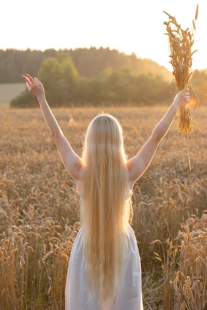 Blonde girl with long hair with raised hands in a wheat field at sunset Soft focus