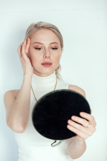 Photo blonde girl with makeup looking in to mirror on white