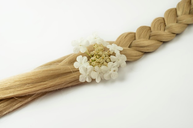 A blonde hair tress with a white flower on it lying on a white background