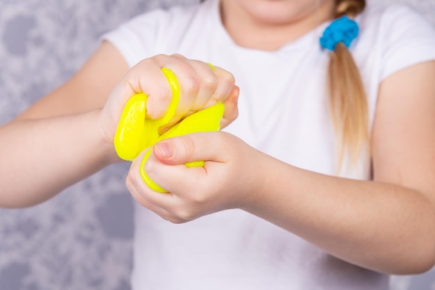 The blonde-haired child is playing with mucus. Little beautiful caucasian girl is playing with yellow slime. Play Slime Toy