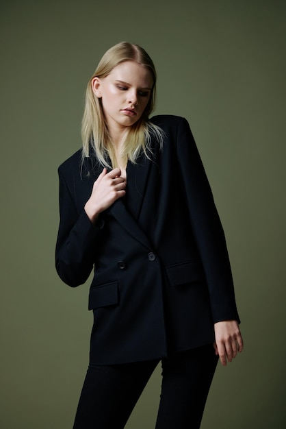 A blonde lady holds a jacket by the collar with one hand posing on a green background in the studio A concept for clothing brands Cool offer for fashionable suits