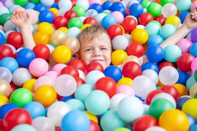 Blonde little boy lying on multi coloured plastic balls in big dry paddling pool in playing centre