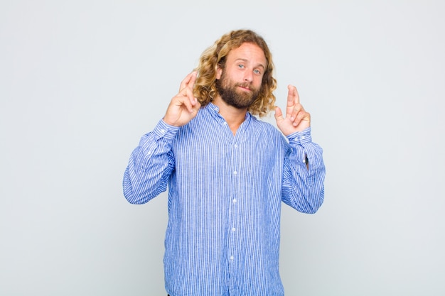 Blonde man crossing fingers anxiously and hoping for good luck with a worried look