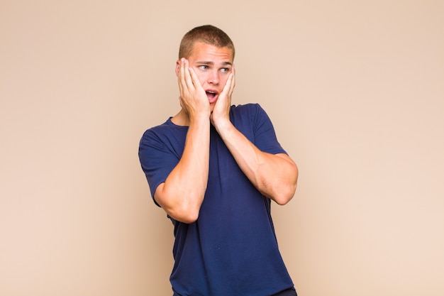 Blonde  man feeling happy, excited and surprised, looking to the side with both hands on face