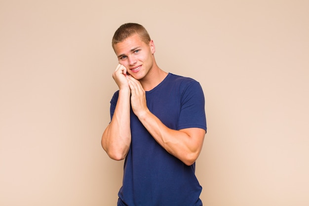 Blonde  man feeling in love and looking cute, adorable and happy, smiling romantically with hands next to face