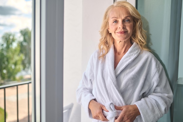 A blonde middle aged woman in a white robe feeling relaxed