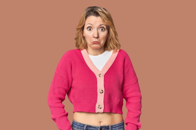 Blonde middleaged Caucasian woman in studio shrugs shoulders and open eyes confused