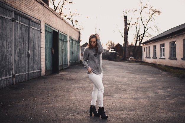 Blonde model girl in white pants, gray sweater and black boots