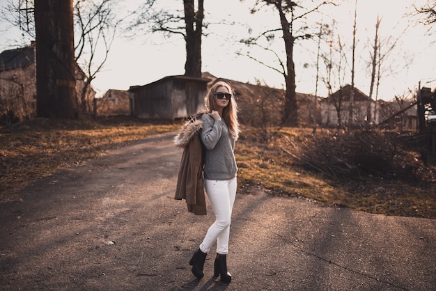 Blonde model girl in white pants, sunglasses, brown coat