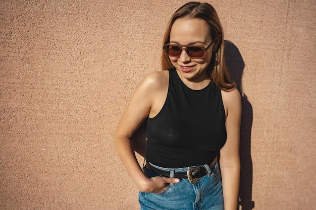 The blonde model wearing sunglasses stands against the beige wall