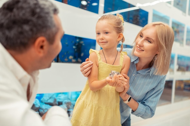 Blonde mom hugging daughter holding hamster in the pet shop