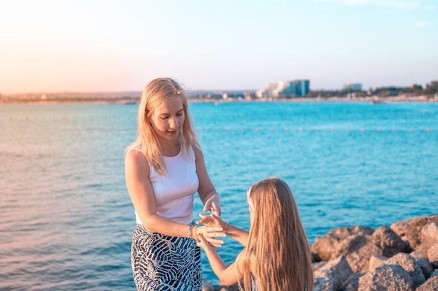 Blonde mother and daughter on the seashore put bracelets on their hands family vacation in the