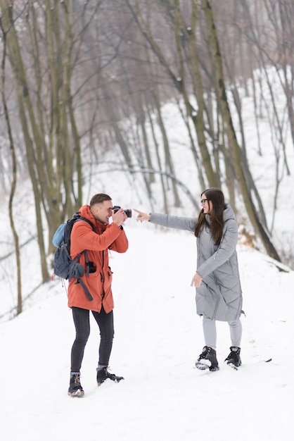 Blonde photograph boy shooting his girlfriend on the winter landscapes background while walking in the forest