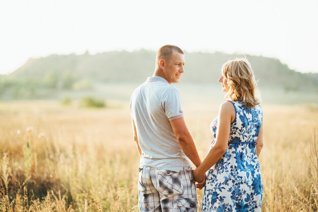 Blonde pregnant girl mom in a blue dress and a man in a field