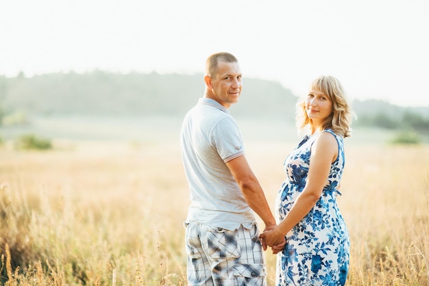 Blonde pregnant girl mom in a blue dress and a man in a field