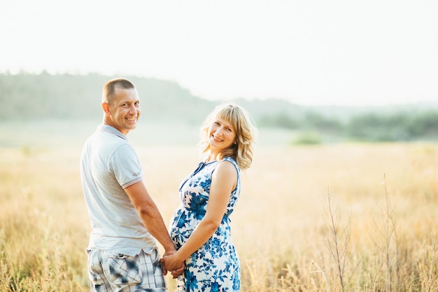 Blonde pregnant girl mom in a blue dress and a man in a field