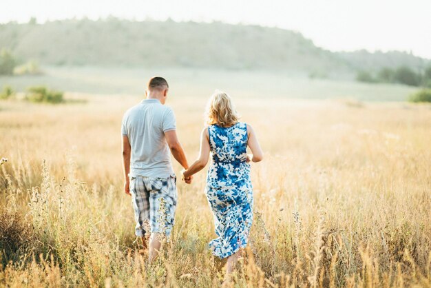 Blonde pregnant girl mom in a blue dress and a man in a field