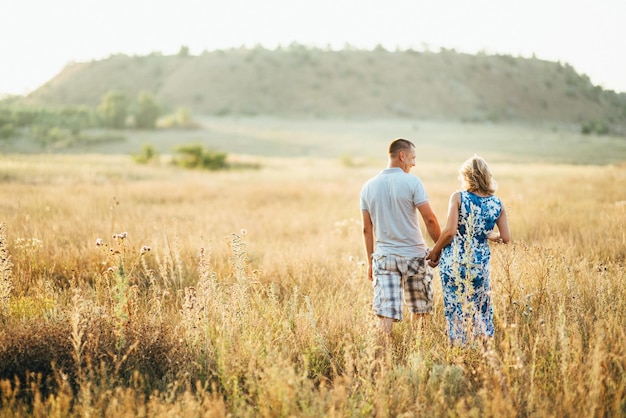 Blonde pregnant girl mom in a blue dress and a man in a field