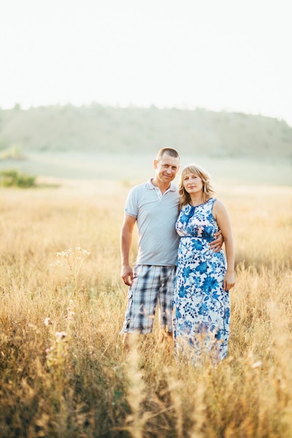 Blonde pregnant girl mom in a blue dress and a man in a field