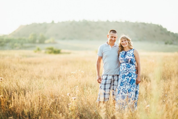 Blonde pregnant girl mom in a blue dress and a man in a field