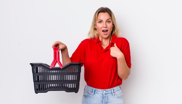 Blonde pretty woman feeling happy and pointing to self with an excited shopping basket concept