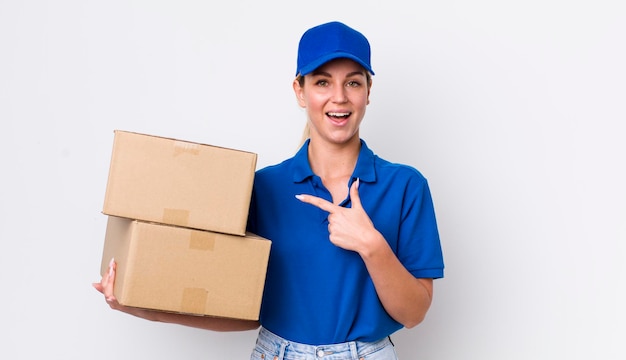 Blonde pretty woman looking excited and surprised pointing to the side shipping boxes concept