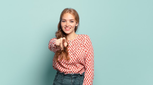 Blonde pretty woman pointing at camera with a satisfied, confident, friendly smile, choosing you