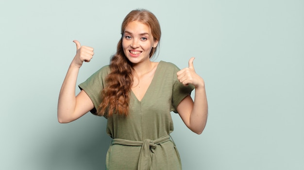 Blonde pretty woman smiling broadly looking happy, positive, confident and successful, with both thumbs up