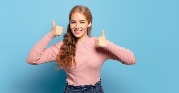 Blonde pretty woman smiling broadly looking happy, positive, confident and successful, with both thumbs up