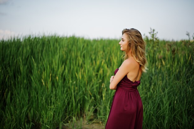 Blonde sensual woman in red marsala dress posing in the reeds.