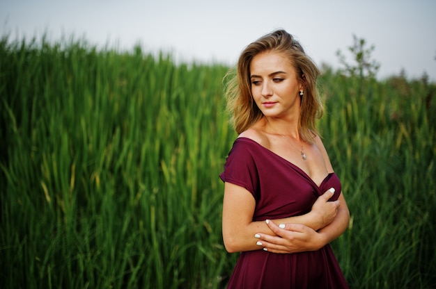 Blonde sensual woman in red marsala dress posing in the reeds.